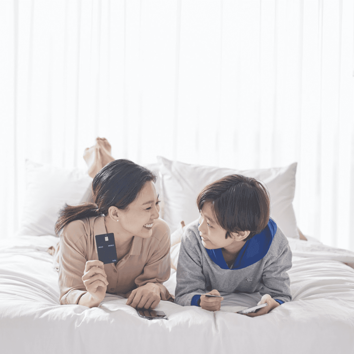 침대에 엎드려 퍼핀카드를 들고있는 엄마와 아들