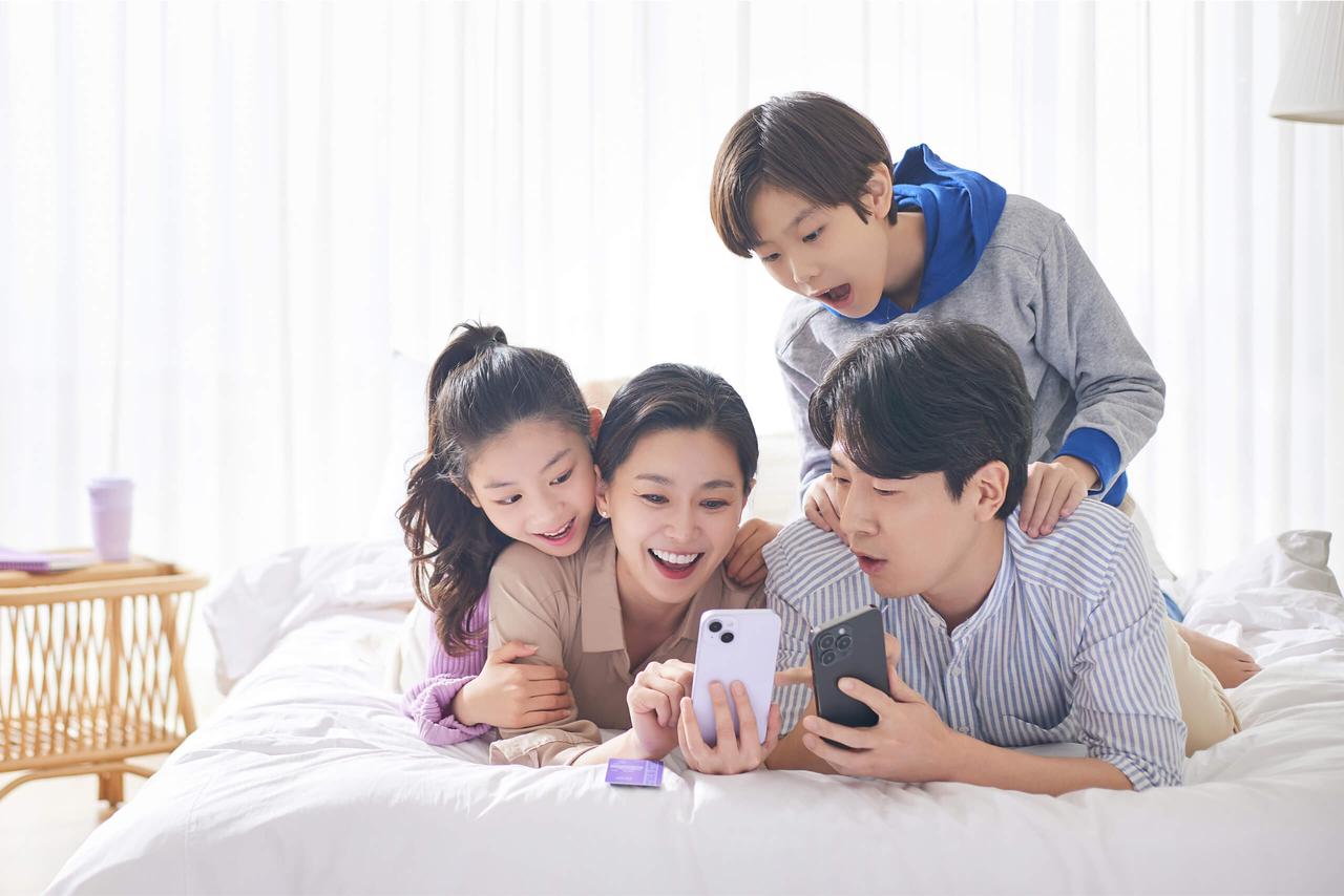 아빠 엄마 아들 딸 네 가족이 침대에서 휴대폰을 보며 즐거운 시간을 보내는 모습
